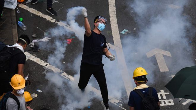 A masked Hong Kong protester throws a tear gas cannister